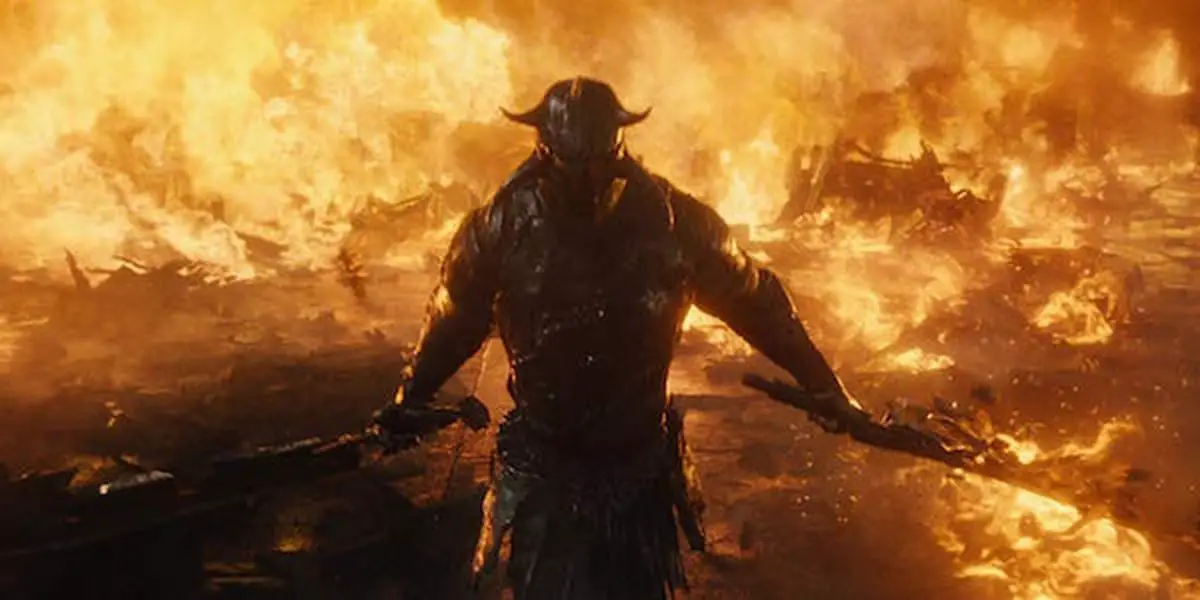 Ares in full armour, weilding two swords walking through a wall of fire.
