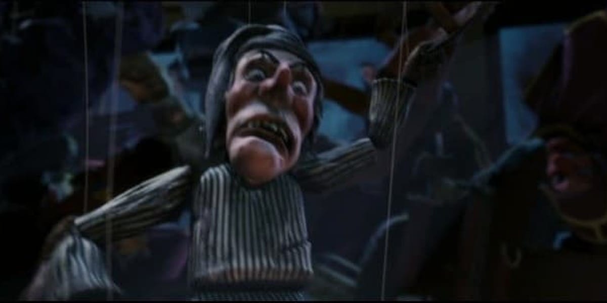 Scrooge puppet one arm down and one arm crooked facing upwards with a dark background in Polar Express