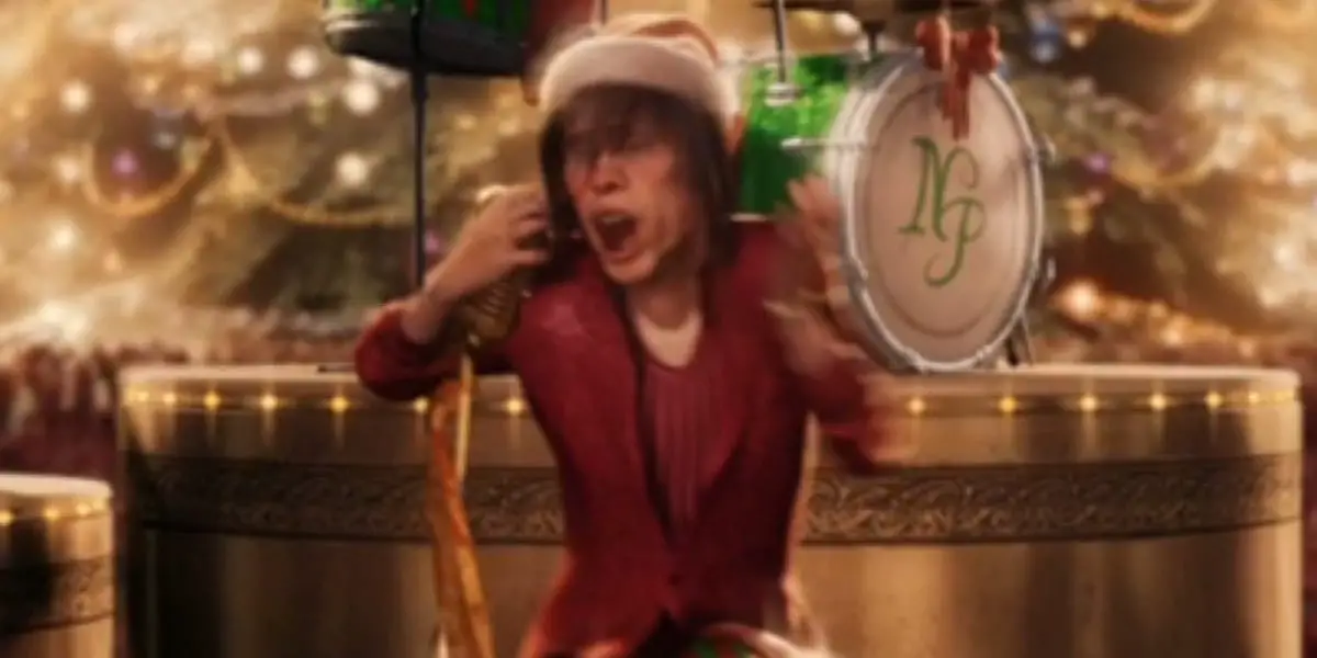 Steven Tyler elf on a unicycle eyes closed mouth open singing into a microphone with lights and decorations behind him in Polar Express