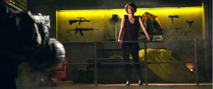 Ma-Ma stands on a balcony surrounded by her personal collection of firearms