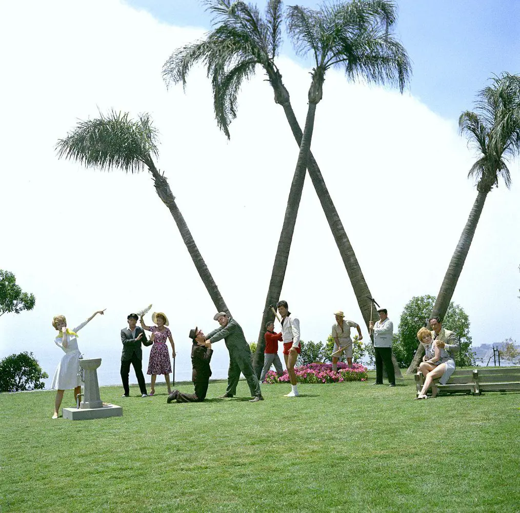 Publicity photo of the cast in character, posed in front of 4 palm trees that form a big W