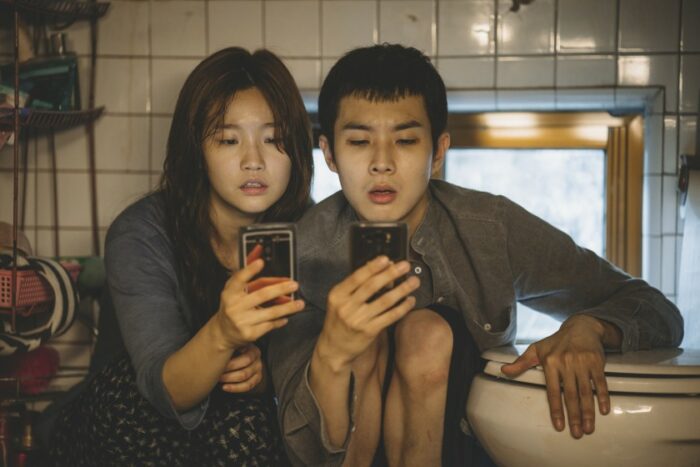 A man and woman sit next to a toilet looking at their phones