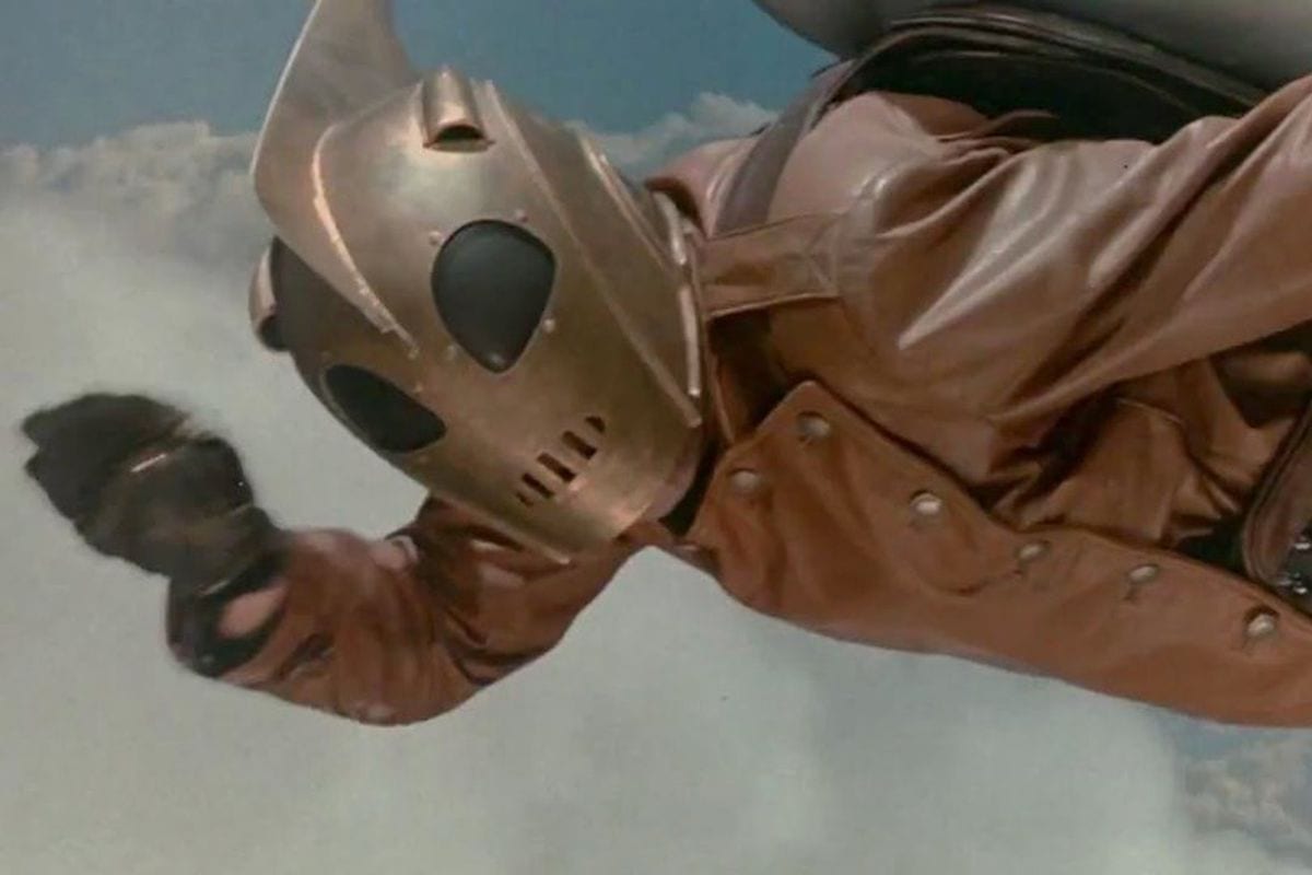 The Rocketeer flying in his iconic helmet and rocket pack. 