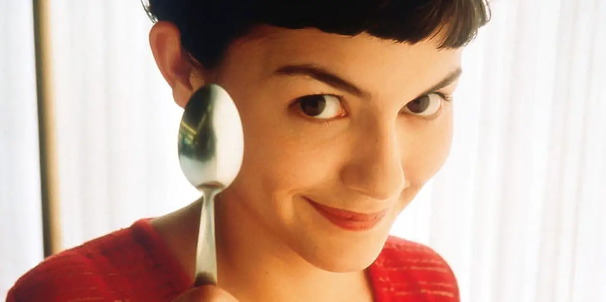 Amelie looking at the camera with a small smile while holding a spoon upwards and straight