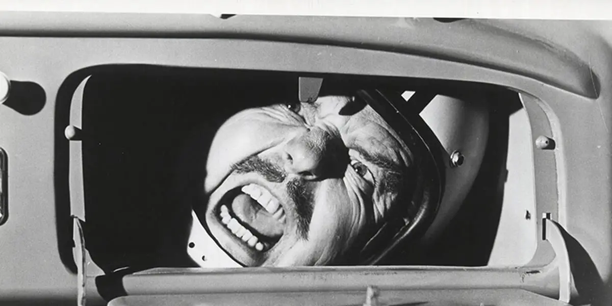 Black and white still of Thorndyke stuck inside Herbie, his mouth open and yelling as his face is visible from the open glove compartment