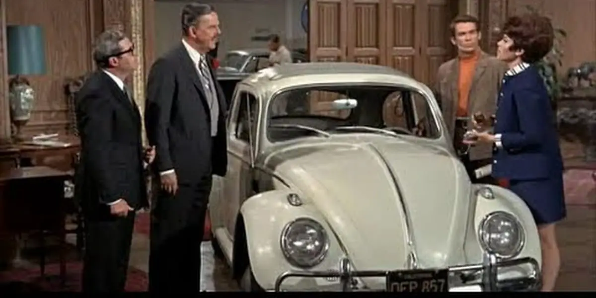Carole, Thorndyke, Havershaw and Jim in Thorndyke's auto showroom with a pearl white Herbie, picture is in color