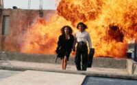 Carolina and El Mariachi walk away from an explosion behind them in an alley below.