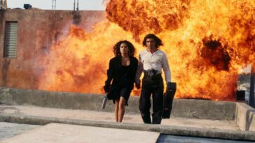 Carolina and El Mariachi walk away from an explosion behind them in an alley below.