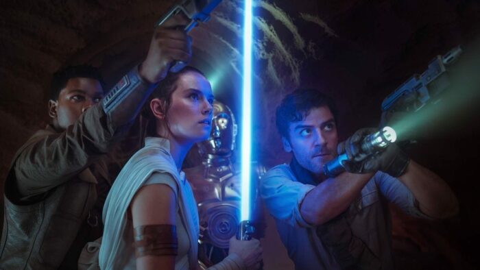 Rey, Poe Dameron, and Finn look up at some unknown threat. C3PO is in the background.