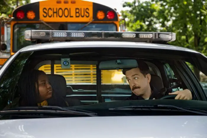 Ed Helms tries to lean towards Kareem Manning while parked in a cop car together.