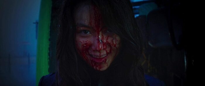 Sook-hee smiles with violent delight with her face covered in blood.