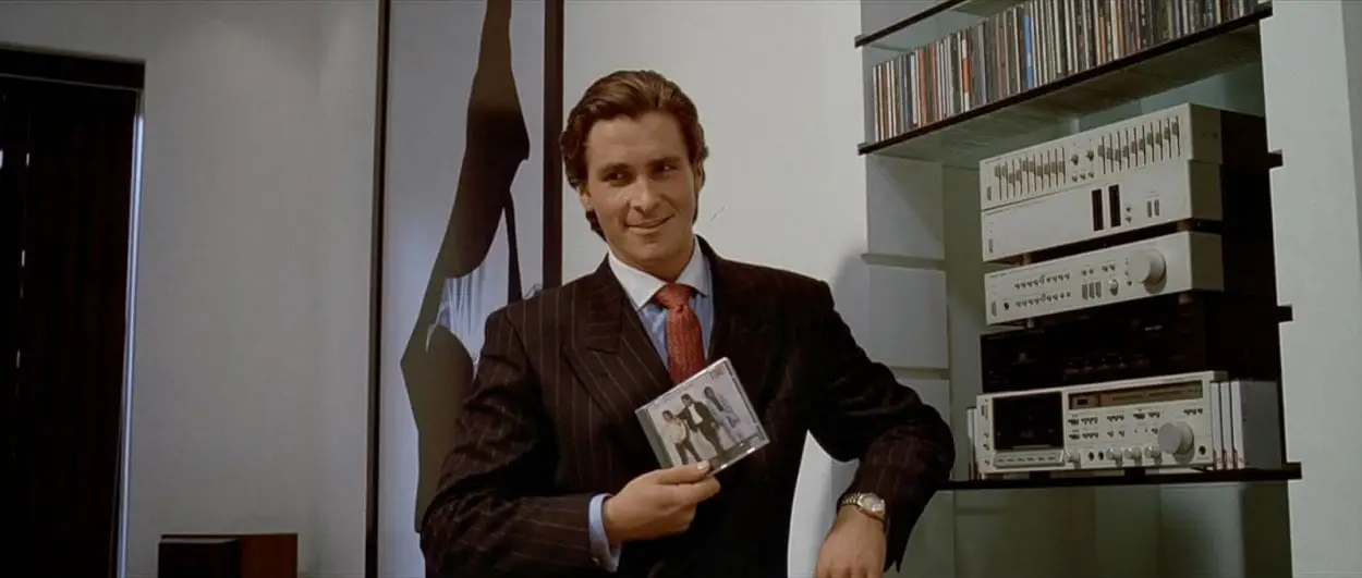 Bateman holds a CD up whilst leaning next to his stereo.