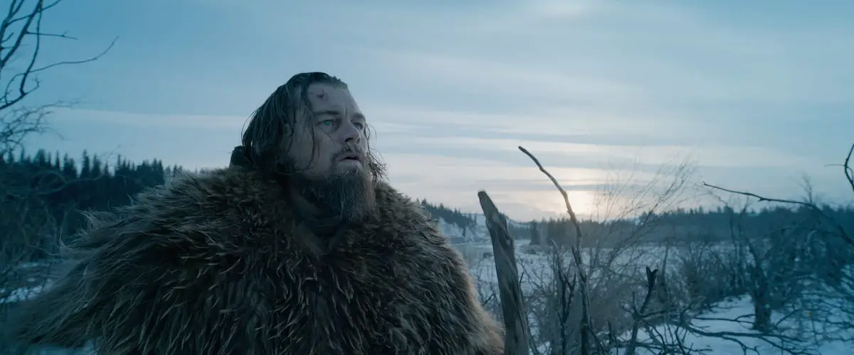 Hugh Glass. clad in a bear fur stands in the middle of a snowy landscape