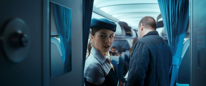 Flight attendant Gökce looks over at Tobias in the cockpit.