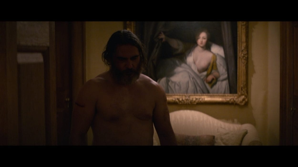Joe shirtless in the Governor's mansion, with the classical female nude framed behind him