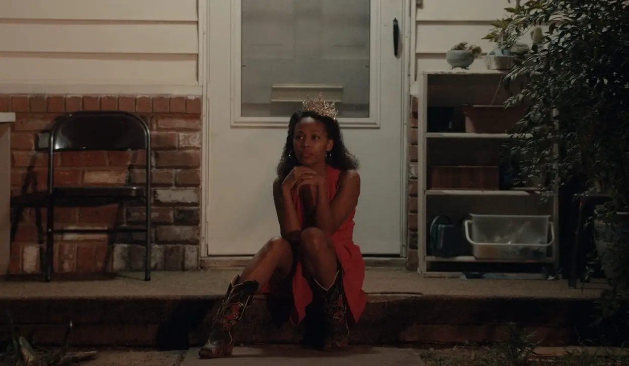 Turquoise Jones sits on her porch wearing a dress, cowboy boots, and her old Miss Juneteenth tiara.