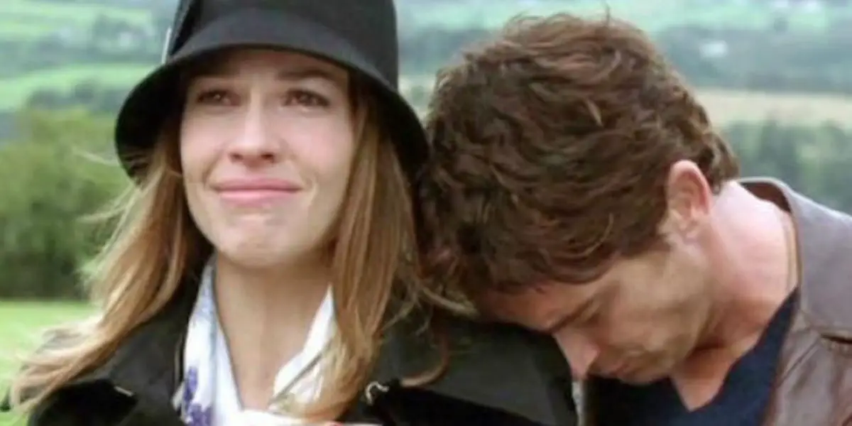 Hilary Swank looking into the distance, smiling yet teary-eyed, with Gerard Butler leaning his head on her shoulder in PS I Love You