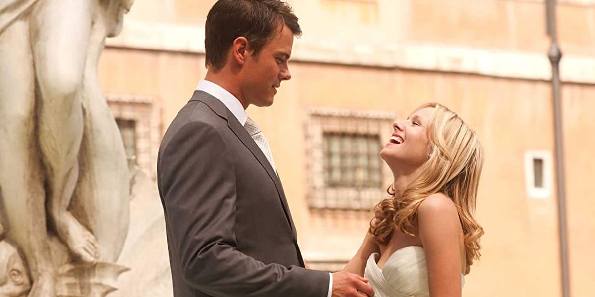 Josh Duhamel looking down at Kristen Bell as she looks up at him laughing and eyes closed in When In Rome dressed for their wedding