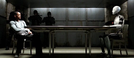 Detective Spooner sits across from Sonny in an interrogation room with armed guards in the background pointing assault rifles in Sonny's direction