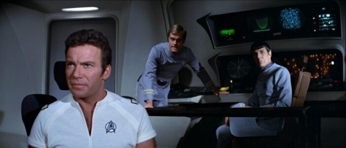 Kirk, a leaning Decker, and a seated Spock look at the viewscreen