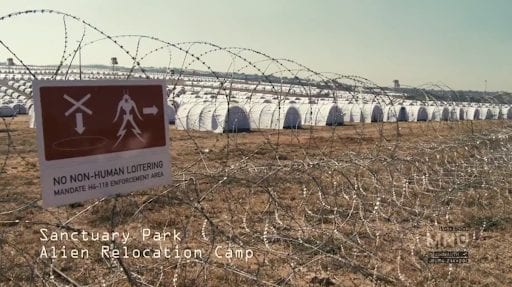 There are many white tents lined up in rows as far as the eye can see, the area is surrounded by barbed