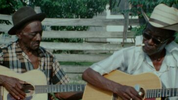 2 older men of colour play acoustic guitar