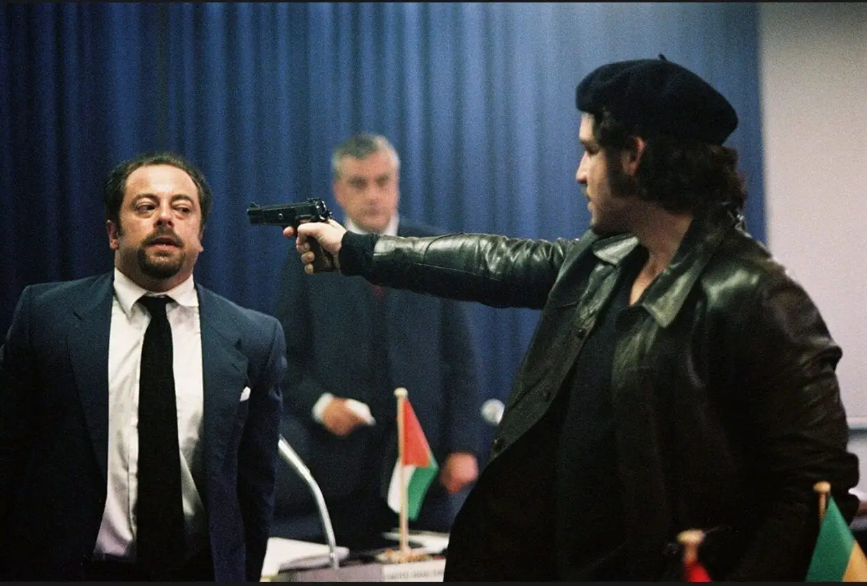 Carlos aims a handgun directly at one of the hostages of the OPEC meeting while another hostage looks on in the background