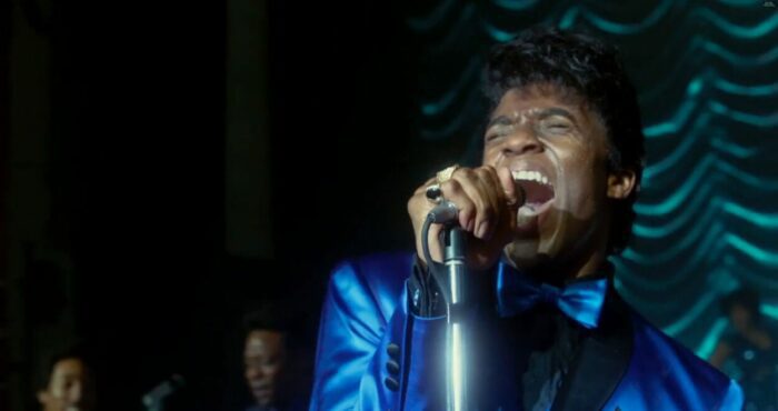 James Brown sings loudly into a microphone with emotional expression.