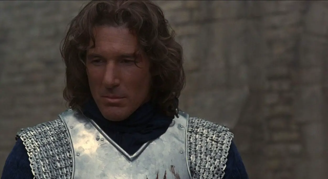 Lancelot stands thinking of a memory while wearing his armor