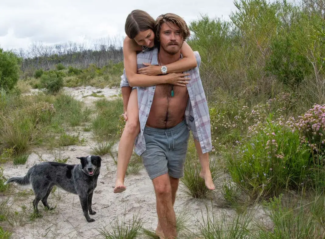 Lu carries Georgie by piggyback down to a beach accompanied by a dog.