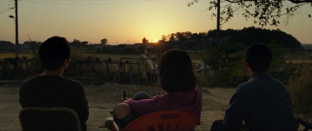 The three characters watch the sunset together with their backs to the camera
