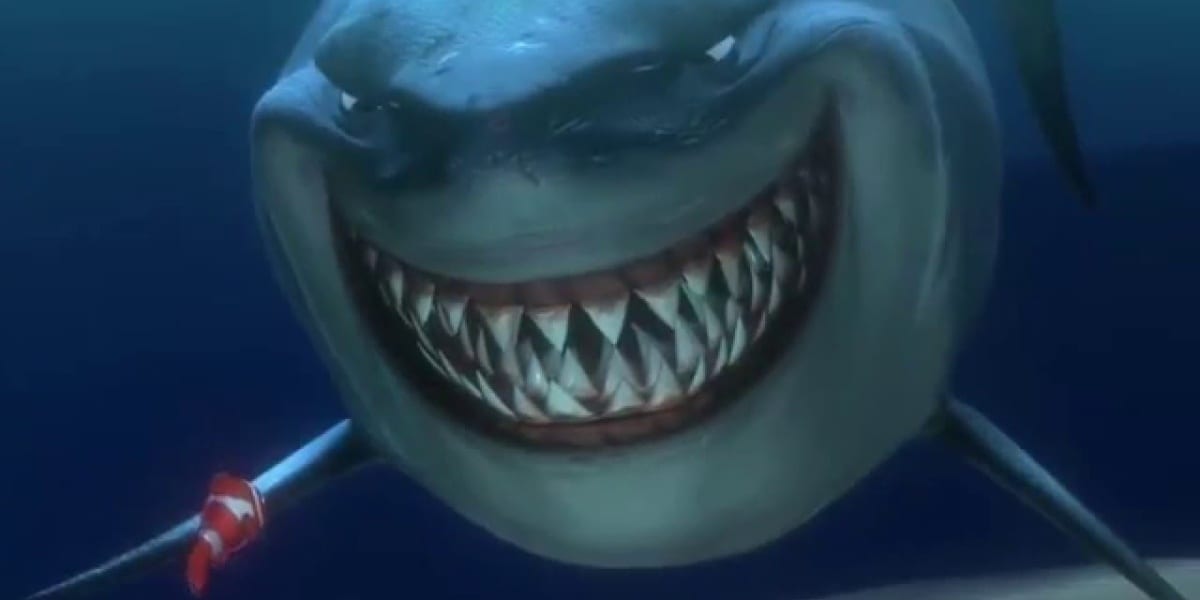 A smiling shark, Bruce, terrifies the living daylights out of Marlin, the clownfish with his back to the photo while under the sea in Finding Nemo