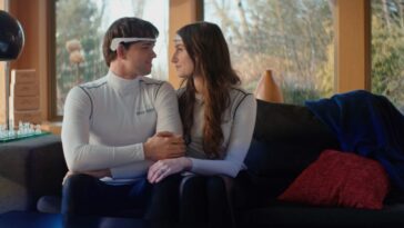 Tom (Jim Schubin) looks longingly into Eve's (Chloe Carroll) eyes as they sit, wearing futuristic brain-mapping headband devices.