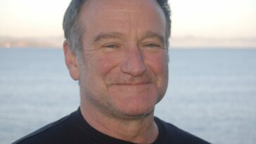 Robin Williams smiling in front of the ocean.