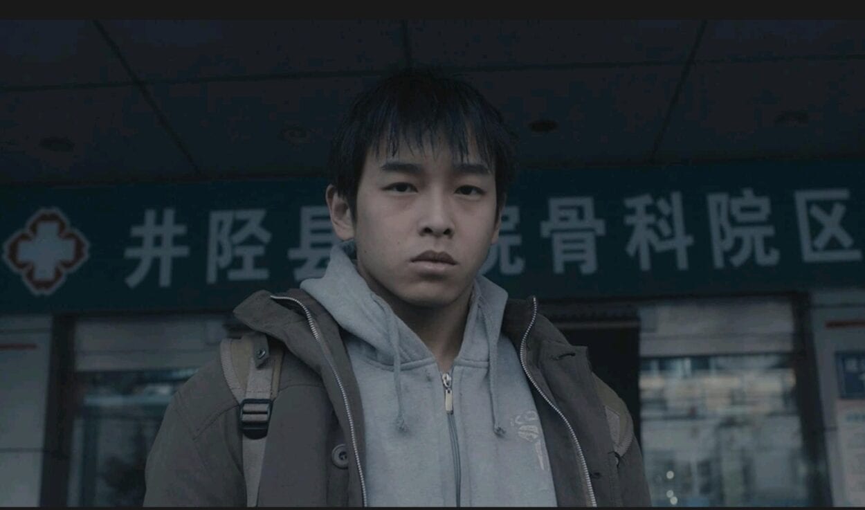 Wei Bu (Yuchang Peng) stands outside the door of a building as he looks into the camera