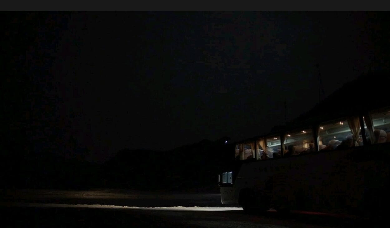 A bus is still in the middle of a dark road with the headlights on