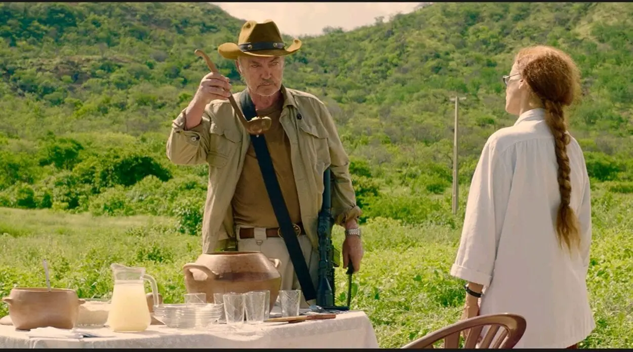 A medium shot of an armed Michael (Udo Kier) and Domingas (Sônia Braga) as they face each other at a table with potted stew and cashew milk