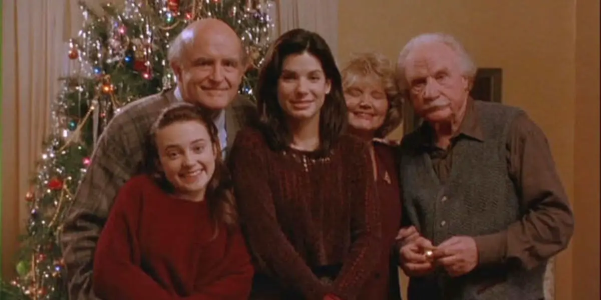 Lucy stands in the middle of a family picture, Peter's parents behind her, his godfather to her left, and Peter's sister to her right with a Christmas tree in the background
