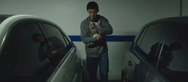 Lee Jong-su, positioned between two cars, holds a cat in his arms