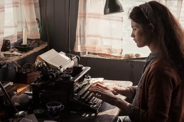 Alice types her latest writing on a typewriter by a window.