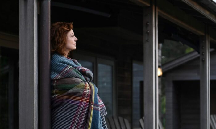Lily stands on her porch wrapped in a blanket and looking towards the beach.
