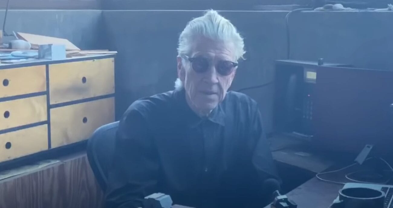 David Lynch sits at his desk wearing dark sunglasses