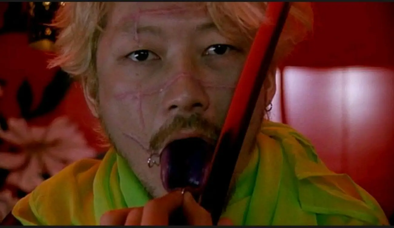 A close-up shot of Kakihara (Tadanobu Asano) as he holds open his pierced tongue while holding a blade on it with his other hand.