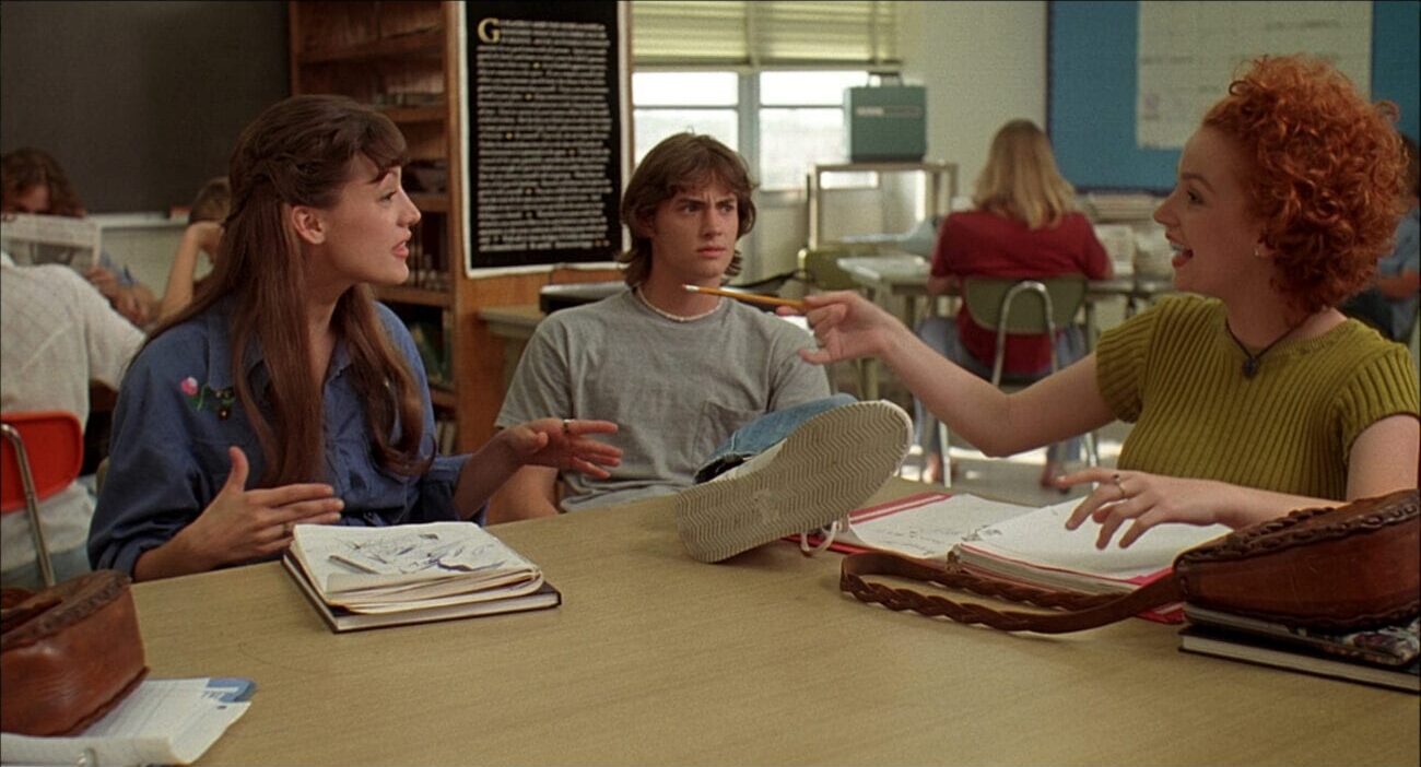 Jodi (Michelle Burke), Pink (Jason London), and Cynthia (Marissa Ribisi) sit in a classroom talking to each other. Pink has his foot on the desk.