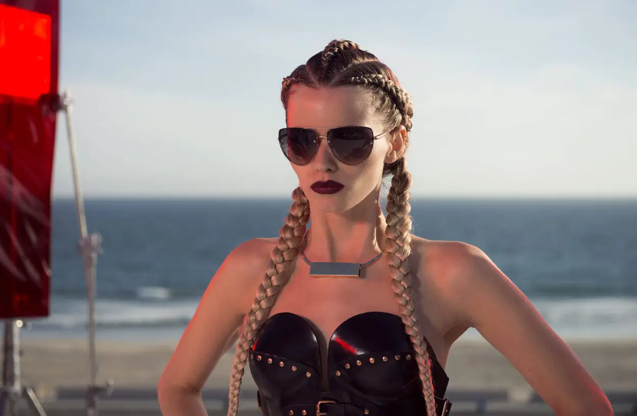 Abbey Lee as Sarah, standing tall and wearing sunglasses
