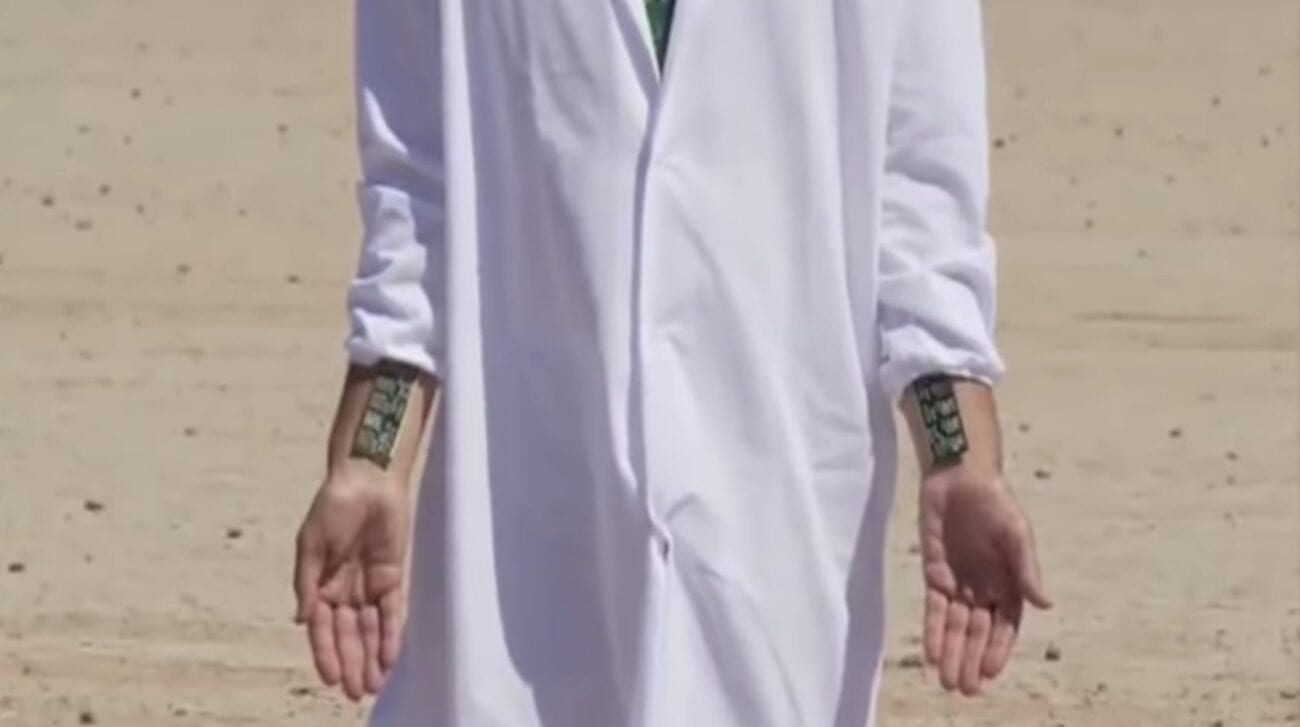 Shot from I Am Here...Now. A shot of Breen's torso clad in a white robe. Circuit breakers are attached to his wrists, mimicking stigmata.