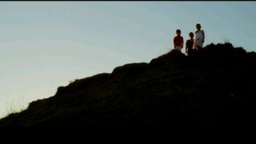 A low-angle shot of Eliza (Angeli Bayani) and her children JR (AJ Baliat) and Sarah (Aneeza Hernandez) looking down from a cliff
