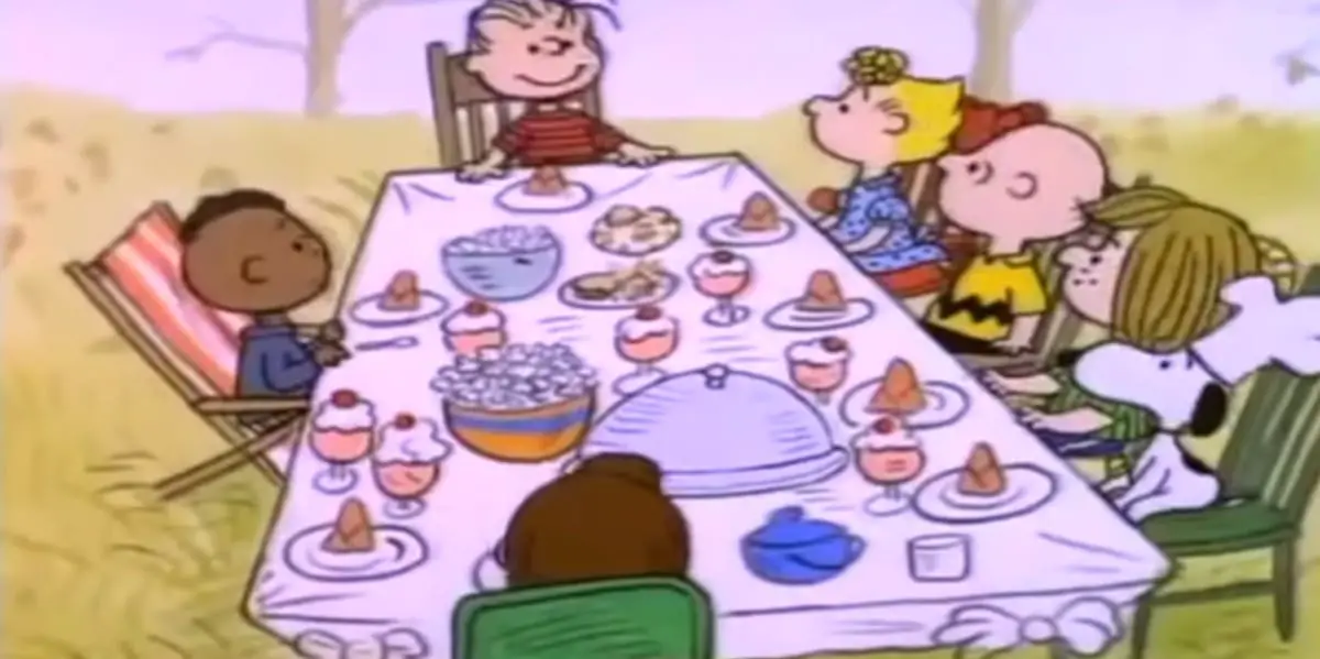 Charlie Brown with Sally, Snoopy, Peppermint Patty, Linus, Franklin and Marcie all sitting at a table in Charlie Brown Thanksgiving