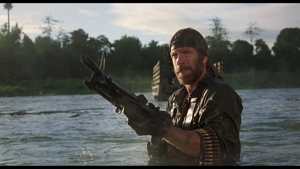 Chuck Norris holding a massive machine gun in a lake in one of many Rambo homages that went straight to video in the '80s