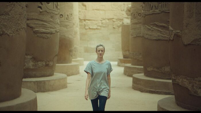 Hana walks between tall hieroglyphic columns
